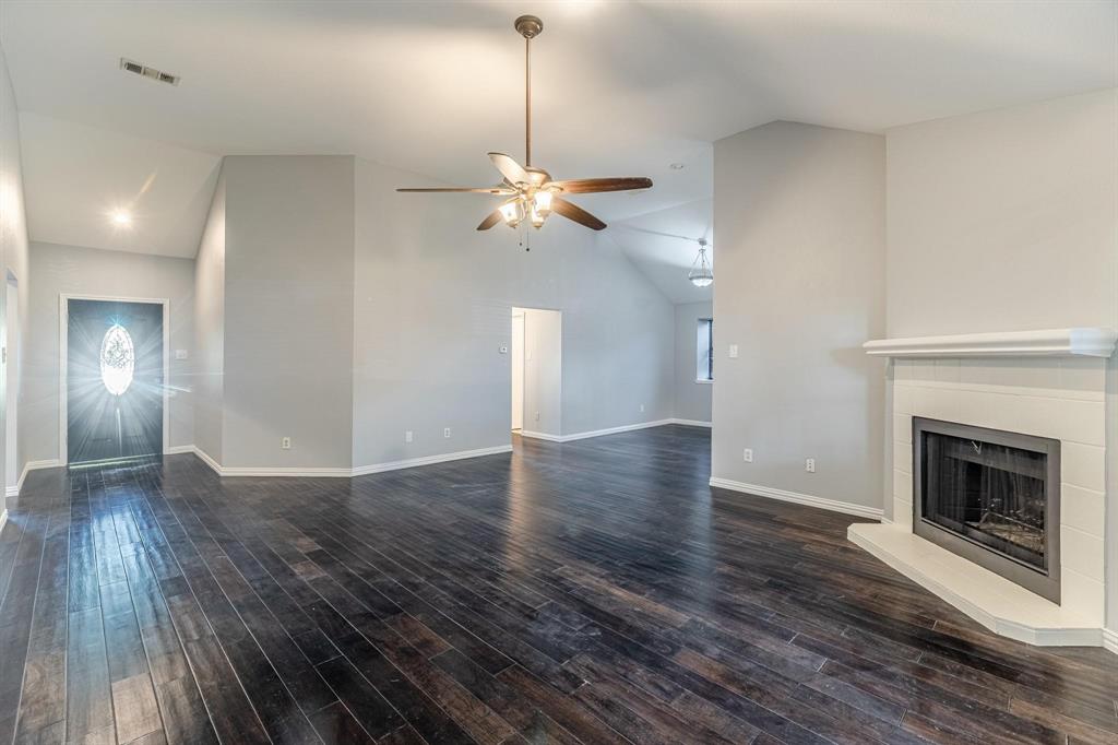 Vaulted ceilings featuring a central ceiling fan, dark wood-finish flooring, and a fireplace with a white tile surround and mantel