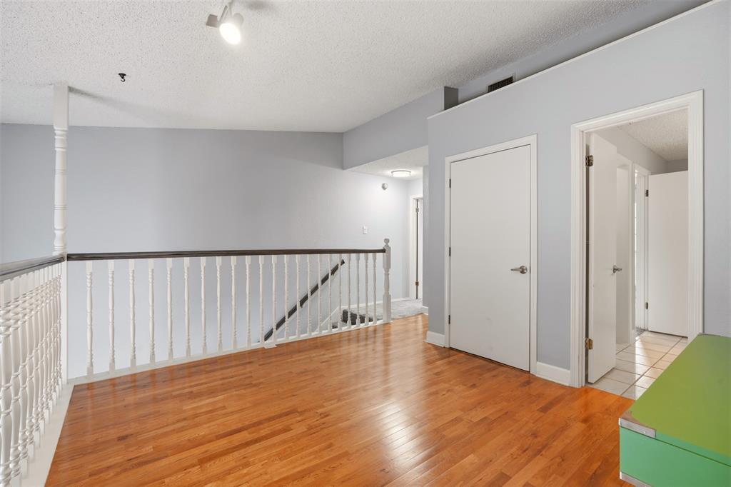 Wood-finish flooring, white spindle staircase railing with a dark wood-finish handrail, and interior doors with brushed nickel hardware