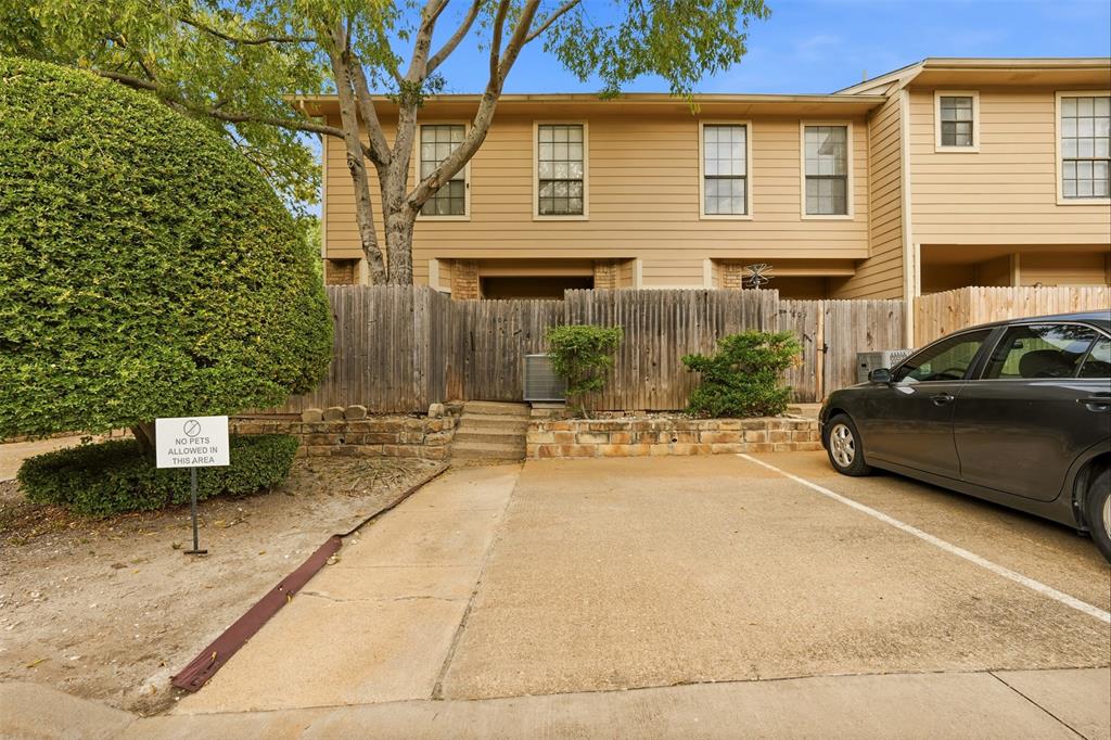 Two-story residence with horizontal siding, dedicated paved parking, stone retaining wall, and wood privacy fencing