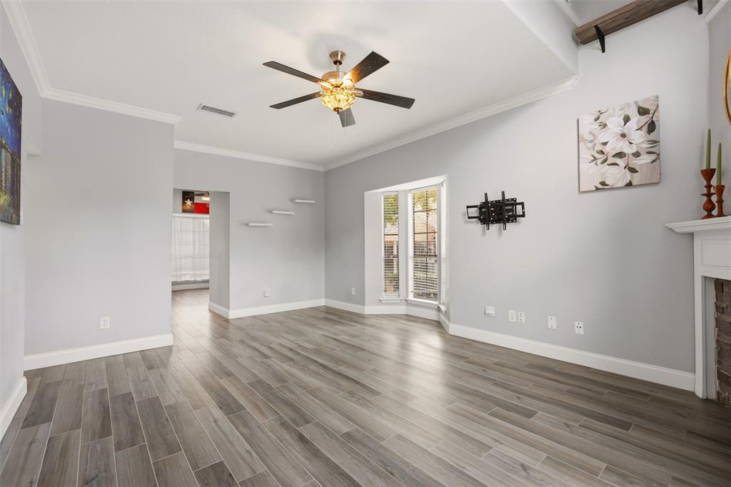 Living area featuring wood-finish tile flooring, a recessed tray ceiling with a multi-blade ceiling fan, a bay window, and a hearth with a brick fireplace surround