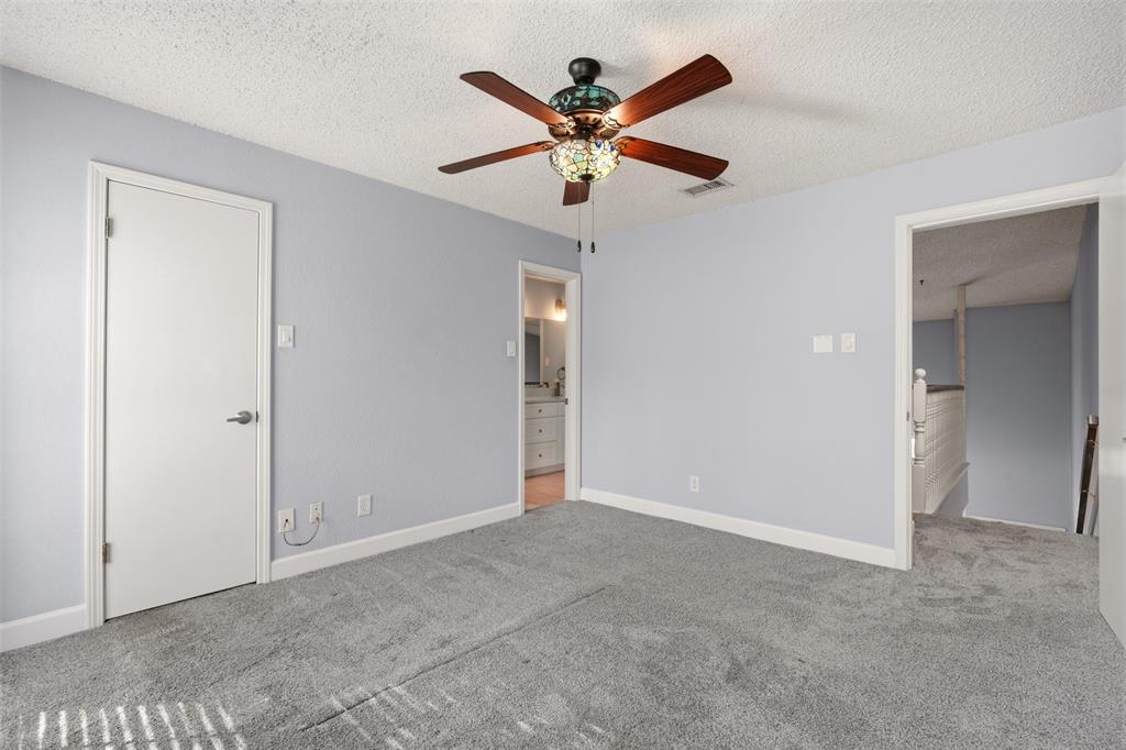 Neutral-toned carpeting, ceiling fan with integrated stained-glass light fixture, and textured ceiling finish