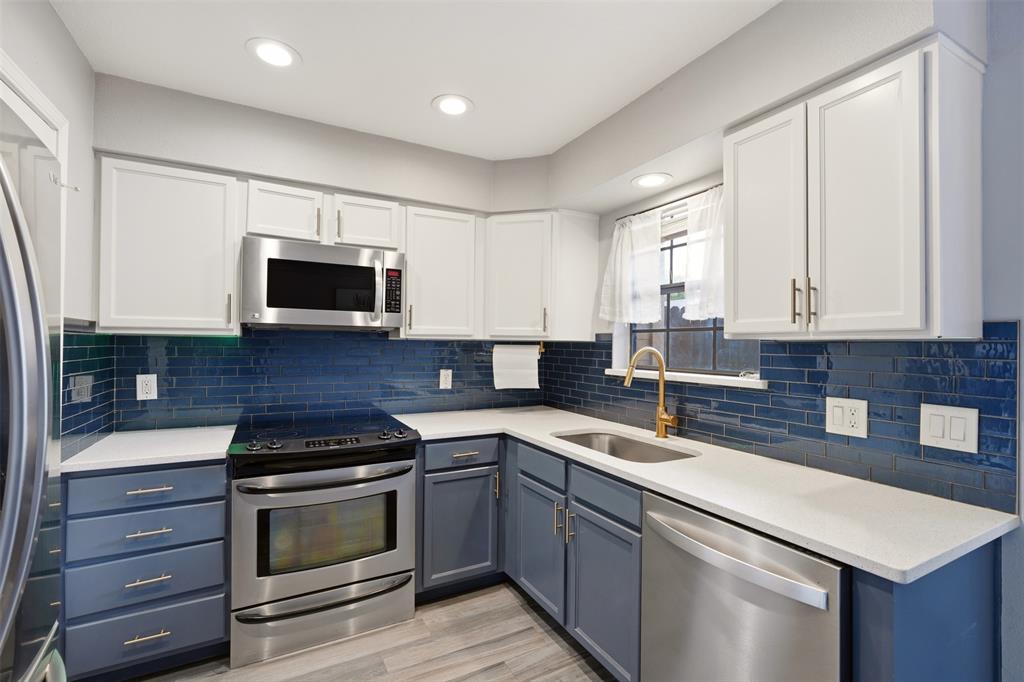 Kitchen featuring two-tone shaker-style cabinetry, deep blue subway tile backsplash, quartz countertops, stainless steel appliances, and a brass-finish faucet