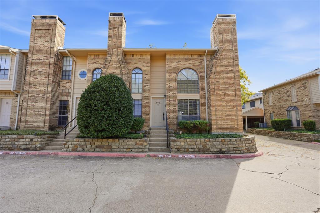Multi-level brick exterior featuring dual masonry chimneys, arched windows, and a stacked stone retaining wall