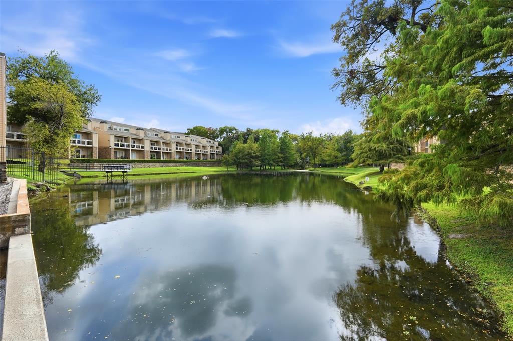 Waterfront pond featuring grassy banks, stone retaining wall, and mature trees