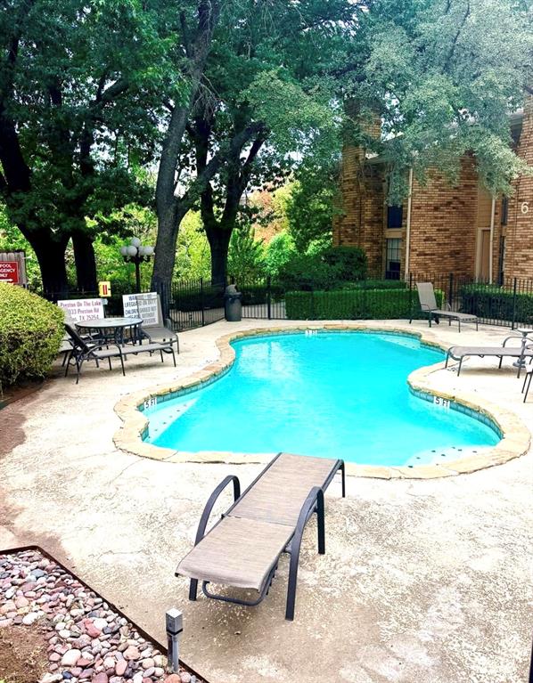 Swimming pool featuring a natural stone coping, concrete decking, metal perimeter fencing, and mature trees