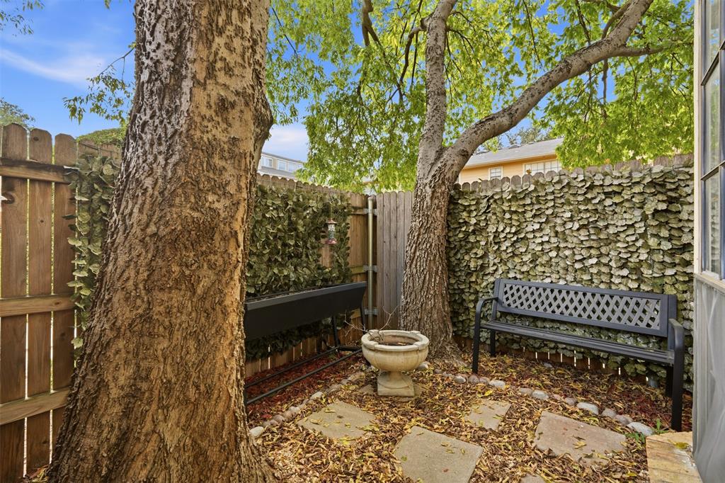 Private outdoor courtyard featuring stone pavers, mature trees, and privacy wood fencing with integrated greenery