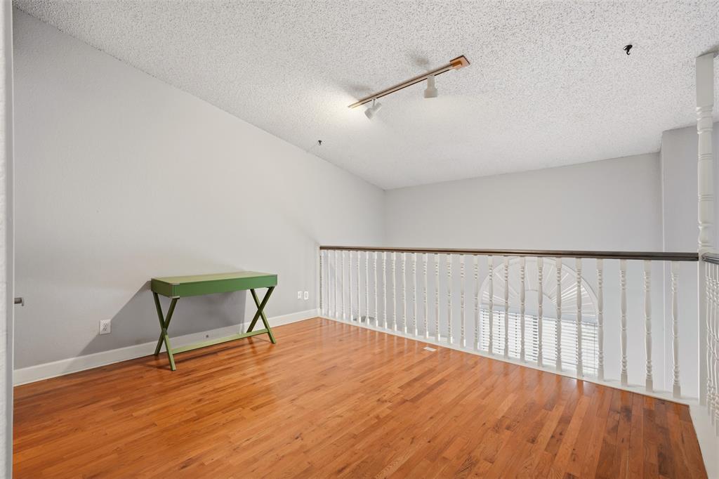 Open-plan space featuring wood-finish flooring, vaulted ceiling, white painted railing with a dark wood-finish cap, and ceiling-mounted track lighting
