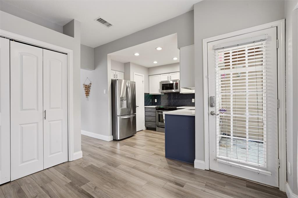 Kitchen featuring stainless steel appliances, dark-toned subway tile backsplash, white shaker-style cabinetry, a contrasting blue base cabinet, and wood-finish flooring