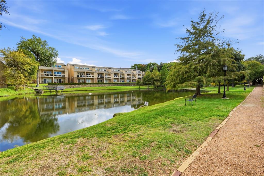 Waterfront grounds featuring a landscaped pond, gravel pathway, mature trees, and stone retaining wall