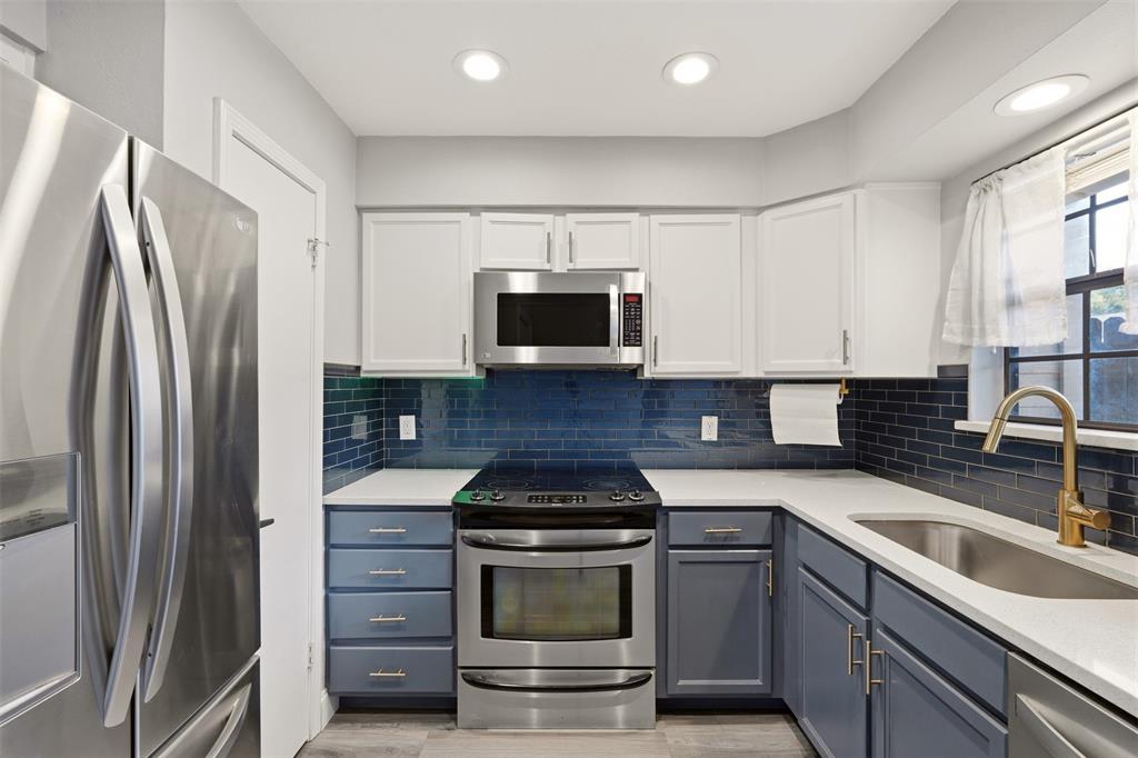 Kitchen featuring white upper cabinetry, blue lower cabinetry, stainless steel appliances, quartz countertops, and blue subway tile backsplash