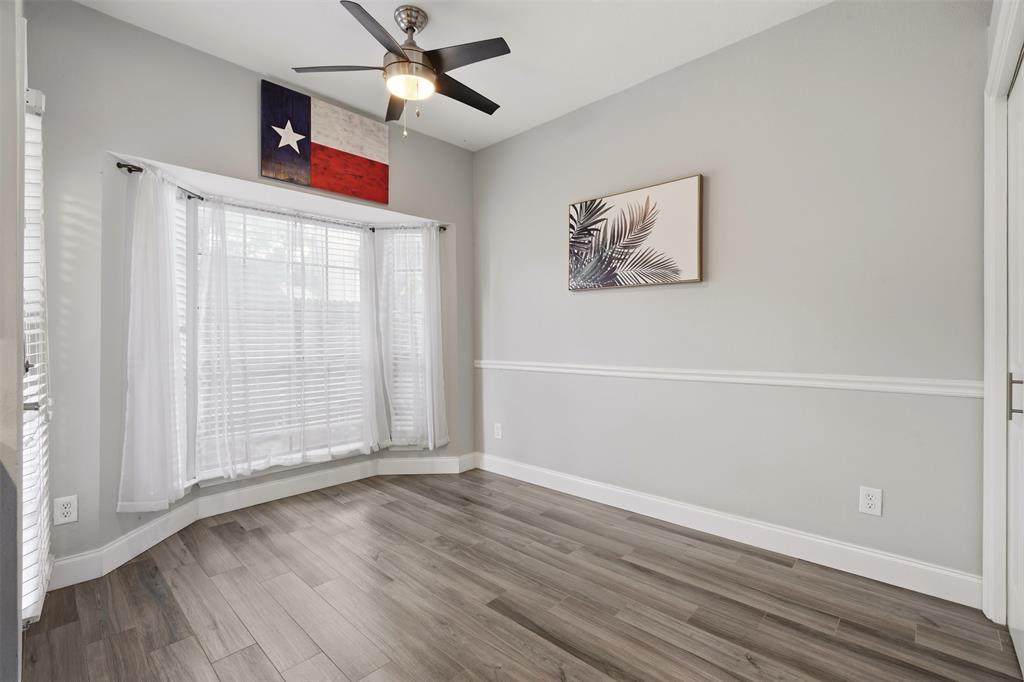 Bay window, wood-finish flooring, chair rail molding, and a multi-blade ceiling fan with integrated lighting