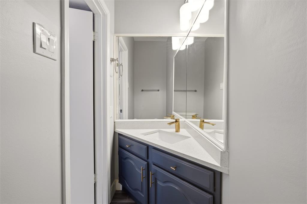 Corner vanity featuring navy cabinetry, stone-composite countertop, integrated sink, gold-tone faucet, and expansive wall mirror