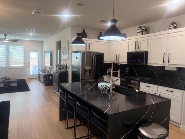 Kitchen featuring a central island with a contrasting stone-surface countertop, white shaker-style cabinetry, matte black hardware, recessed lighting, and wood-finish flooring Kitchen featuring a central island with a contrasting stone-surface countertop, white shaker-style cabinetry, matte black hardware, recessed lighting, and wood-finish flooring