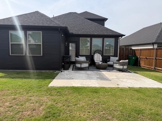 Exterior rear elevation featuring dark-toned siding, a multi-faceted roofline with asphalt shingles, a concrete patio, and a wood privacy fence