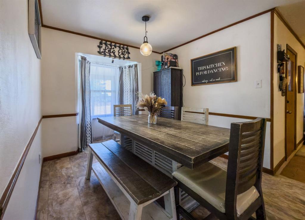 Dining area featuring a bay window, tile flooring, wood-toned chair rail molding, and a pendant light fixture Dining area featuring a bay window, tile flooring, wood-toned chair rail molding, and a pendant light fixture