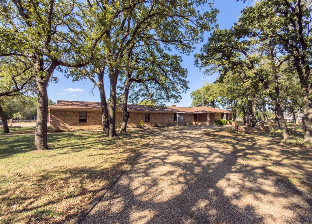 Single-story brick exterior residence featuring a sprawling gravel driveway and mature, expansive tree canopy Single-story brick exterior residence featuring a sprawling gravel driveway and mature, expansive tree canopy