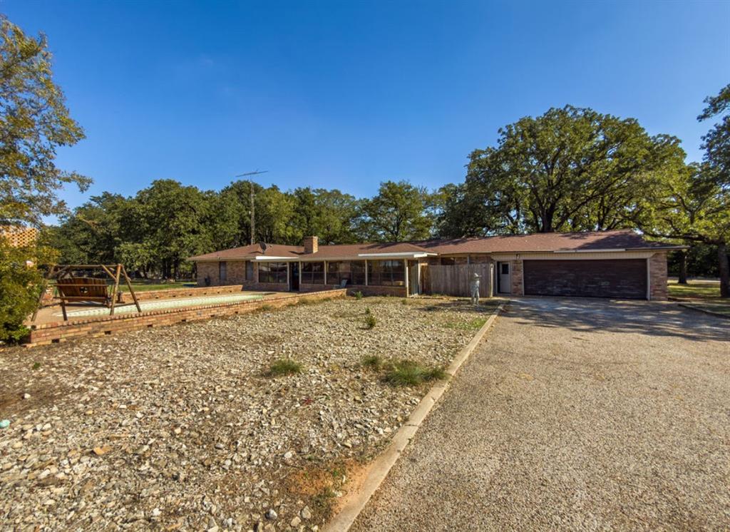 Single-story brick exterior featuring a multi-car garage, expansive graveled grounds, and a raised brick-bordered patio area