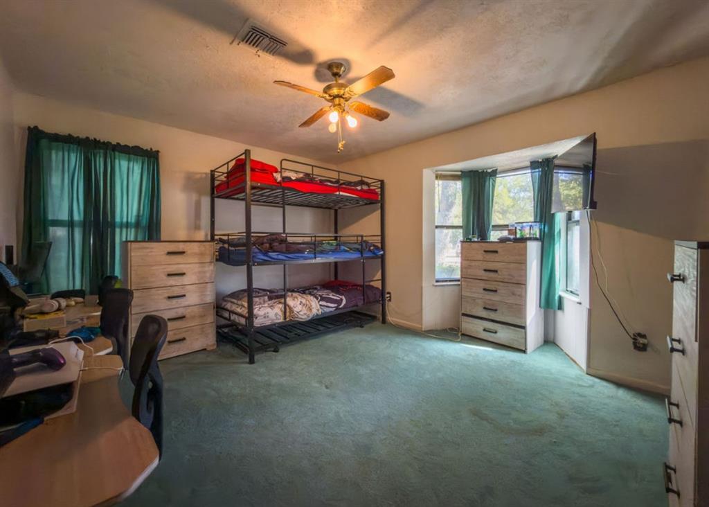 Bedroom featuring wall-to-wall carpeting, a multi-pane bay window, and a ceiling-mounted light fixture with an integrated fan