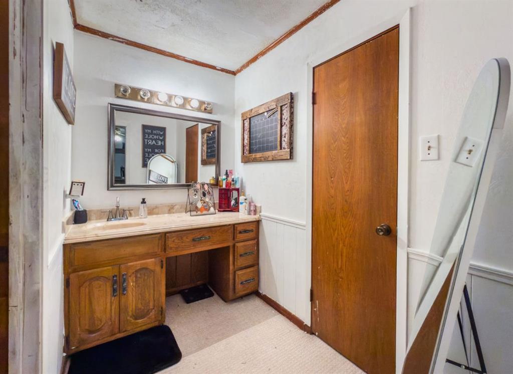 Bathroom vanity with stone-finish countertop, integrated sink, and wood-finish cabinetry, featuring a framed mirror, five-bulb vanity light fixture, and wood-finish interior door