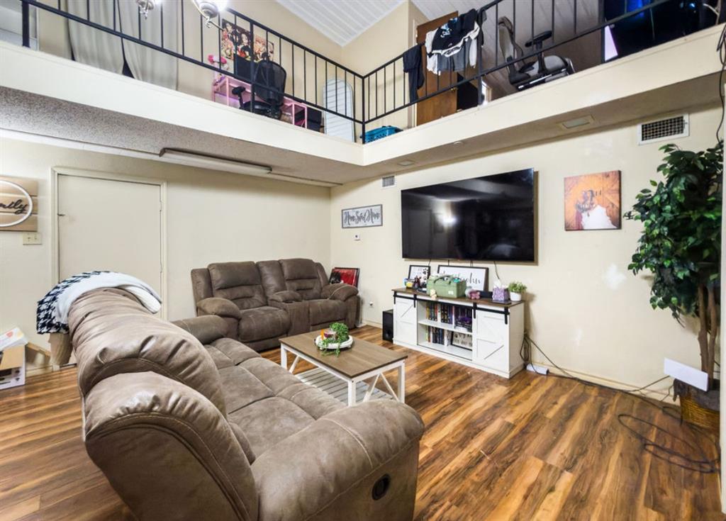 Living area featuring vaulted ceilings, wood-finish flooring, and a second-level interior balcony with black metal railing