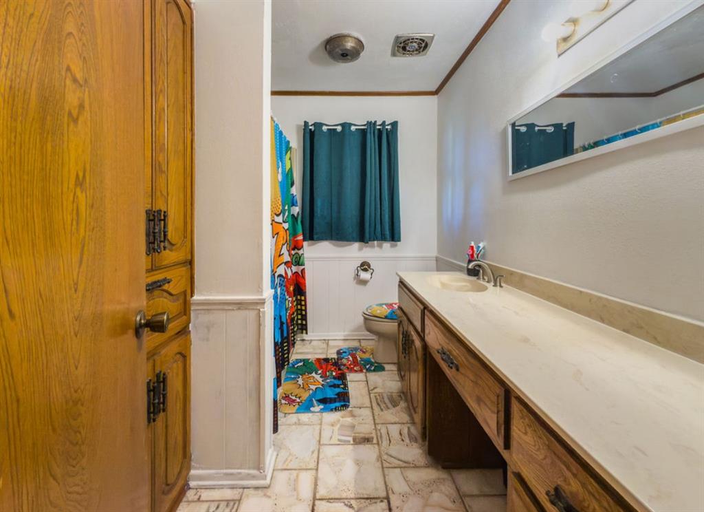Bathroom featuring wood-finish cabinetry, long integrated vanity countertop, tiled flooring, beadboard wainscoting, and a wall-mounted rectangular mirror