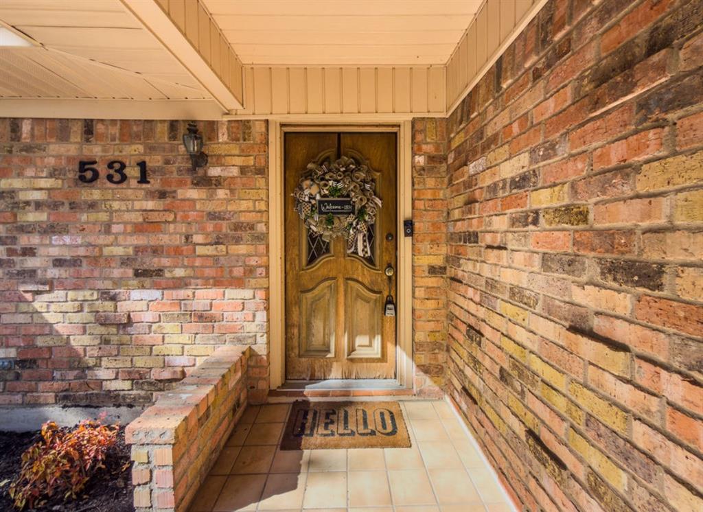Covered entryway featuring a natural brick facade, solid wood double doors with inset glass detailing, tile flooring, and integrated address numerals