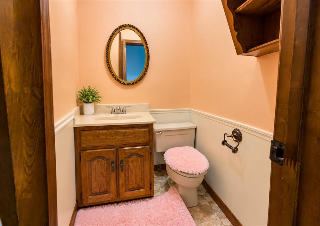 Wood cabinetry vanity featuring a solid surface countertop, an oval wall-mounted mirror with an ornate frame, built-in wooden shelving, and decorative chair rail trim