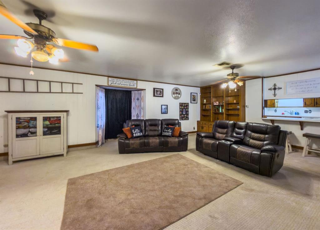 Spacious room featuring wood-finish built-in shelving, two ceiling fans with integrated light fixtures, and a pass-through opening to additional living space Spacious room featuring wood-finish built-in shelving, two ceiling fans with integrated light fixtures, and a pass-through opening to additional living space