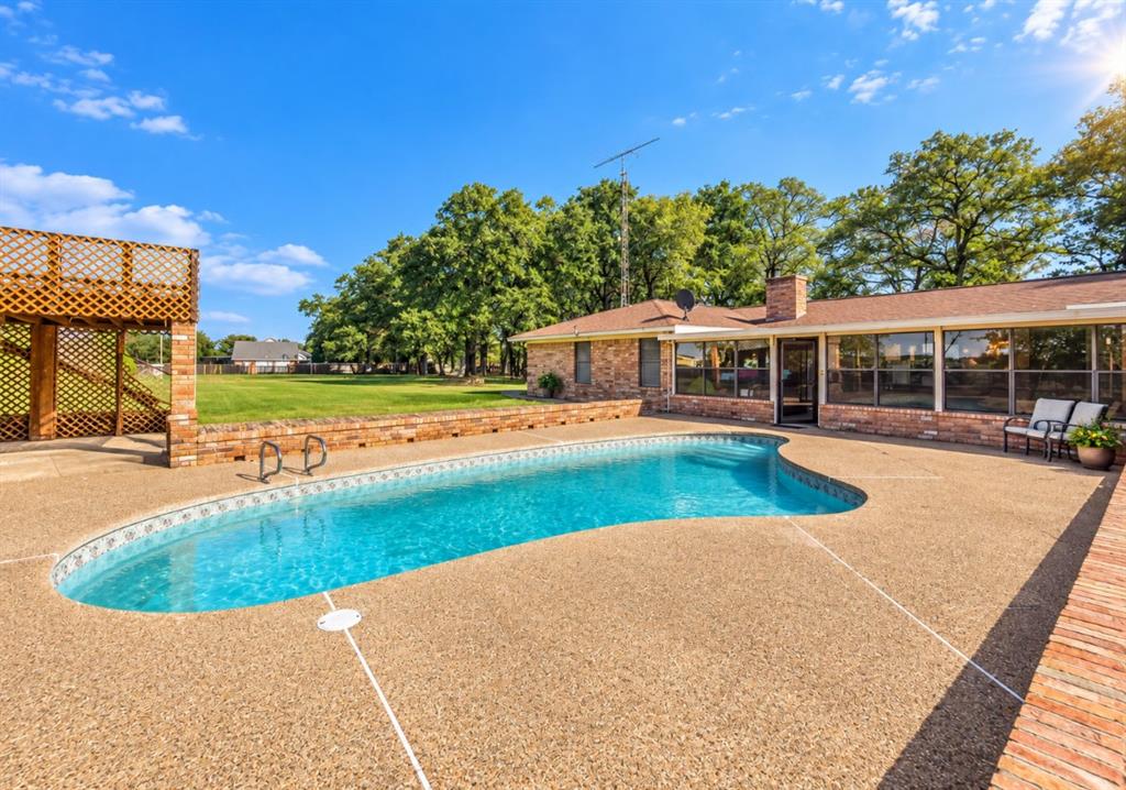 Brick exterior residence featuring an in-ground pool, expansive aggregate decking, multi-level wood lattice deck, and a brick privacy wall