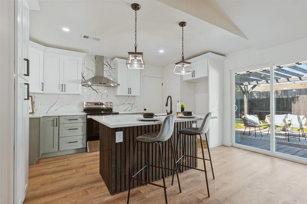 Kitchen featuring shaker-style cabinetry, a central island with vertical wood detailing, a stone-patterned backsplash, stainless steel appliances, and wood-finish flooring