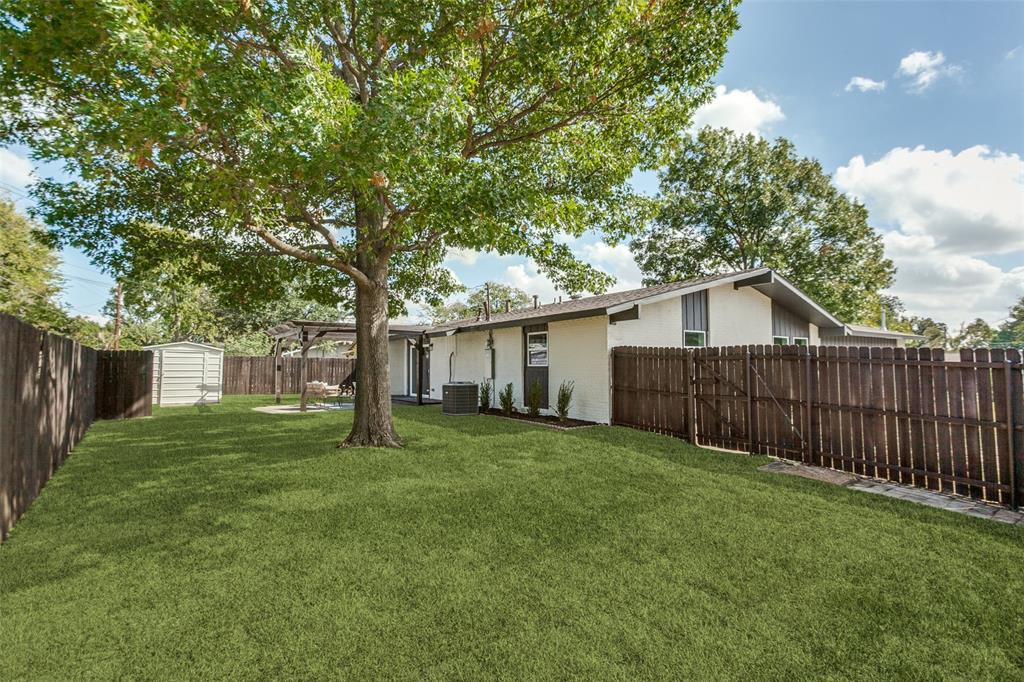 Rear exterior featuring a spacious fenced yard, mature trees, a covered patio area, and a detached storage structure
