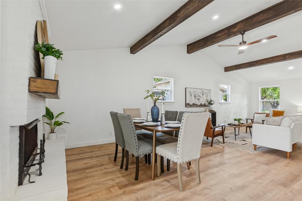 Vaulted ceilings featuring exposed wood beams, white painted brick fireplace, and wood-finish flooring
