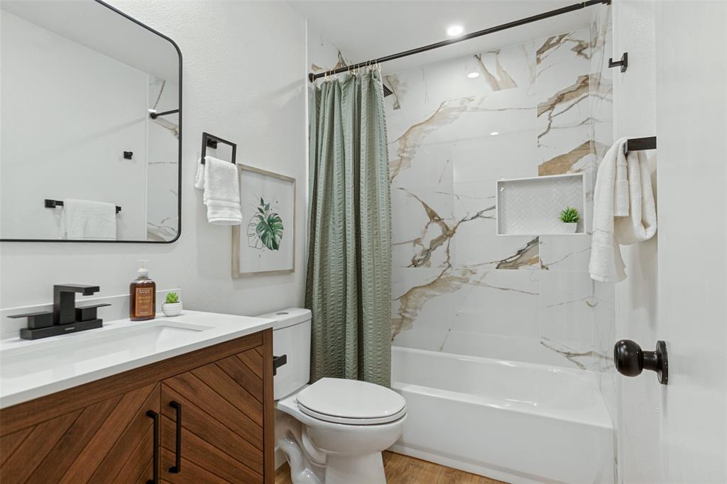 Bathroom featuring a wood-finish vanity with a rectangular sink, matte black faucet, wall-mounted mirror, and tub surround with decorative stone-patterned tile and a recessed niche