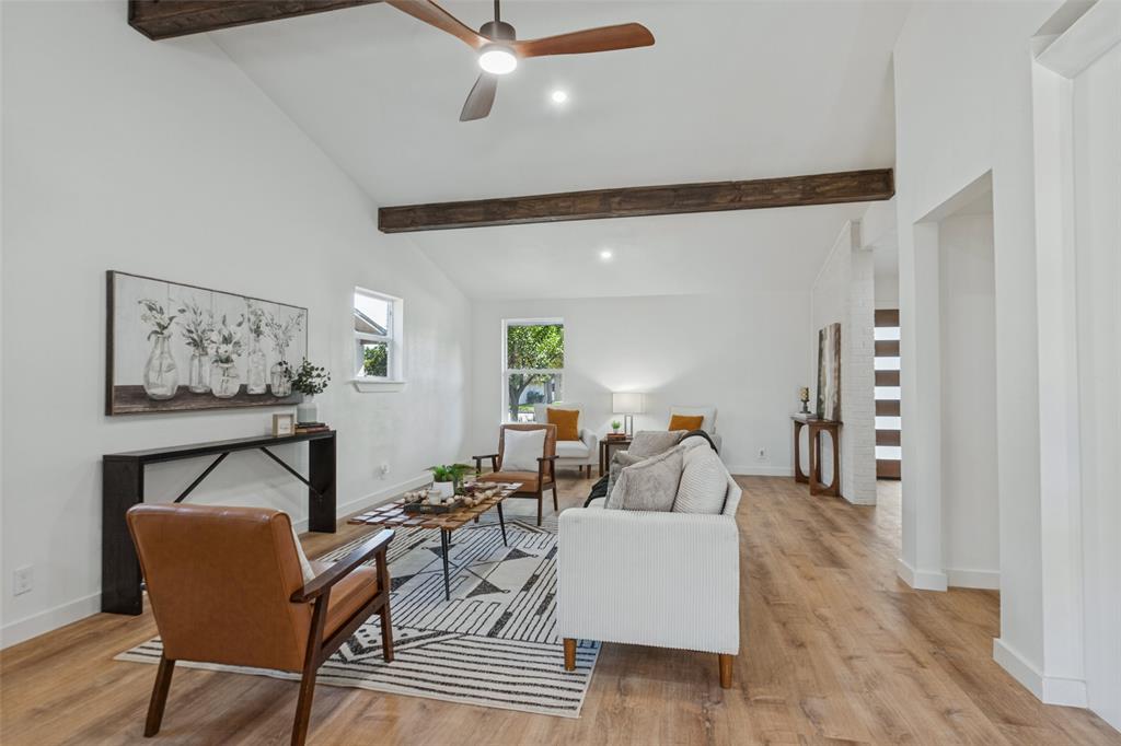 Vaulted ceiling featuring exposed timber beams, wood-finish flooring, and a ceiling fan with integrated lighting