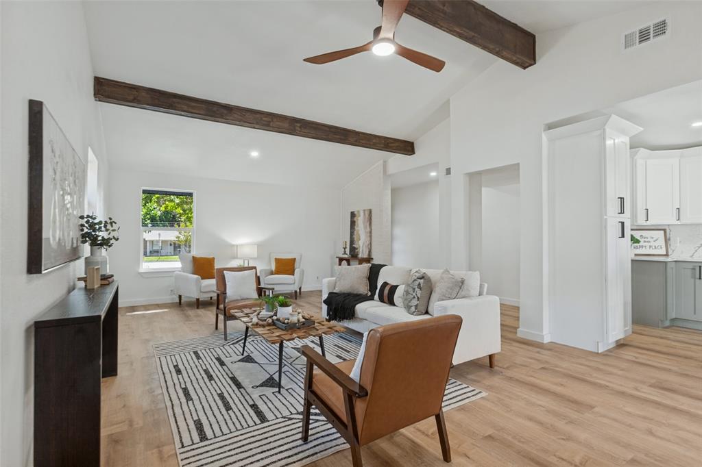 Open-concept room featuring vaulted ceilings, dark wood-finish ceiling beams, wood-finish flooring, and a modern three-blade ceiling fan