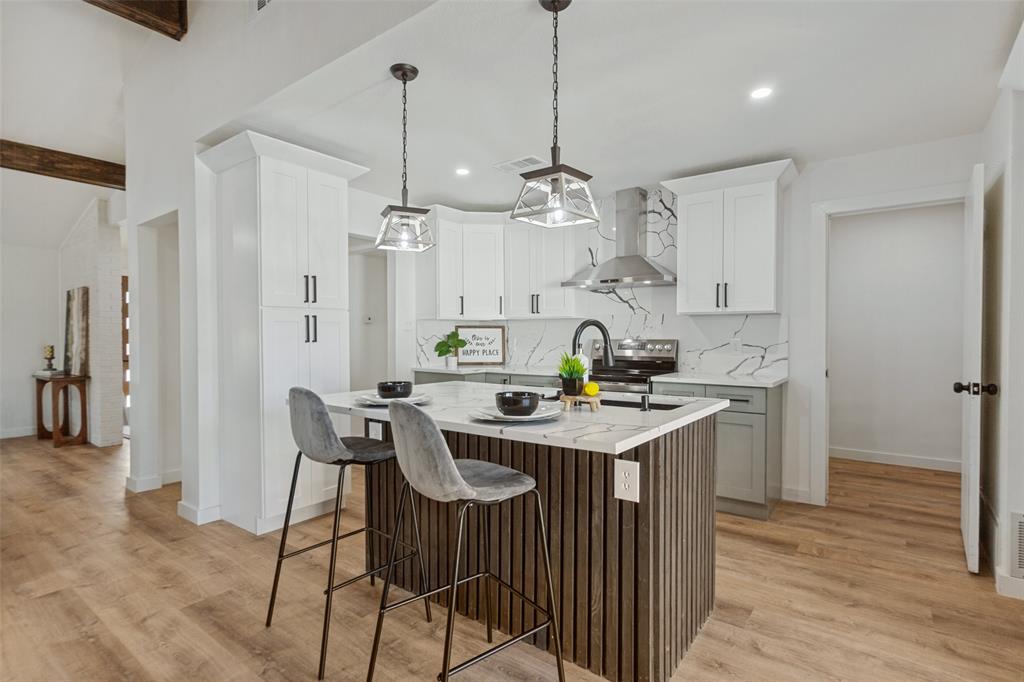Kitchen featuring white shaker-style cabinetry, quartz countertops with integrated backsplash, wood-finish flooring, a vertical-slat kitchen island, and dual pendant lighting