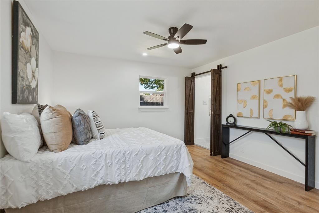 Interior room featuring wood-finish flooring, a five-blade ceiling fan with integrated lighting, and dark wood-finish sliding barn doors