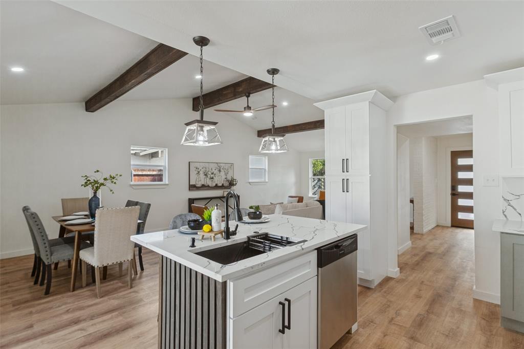 Kitchen featuring a central island with a stone-patterned countertop, dark metal hardware, wood-finish flooring, exposed ceiling beams, and pendant lighting