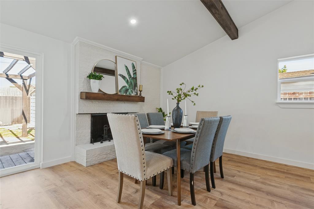 White-painted brick fireplace with a wood mantel, wood-finish flooring, vaulted ceiling featuring a decorative exposed wood beam, and glass patio door