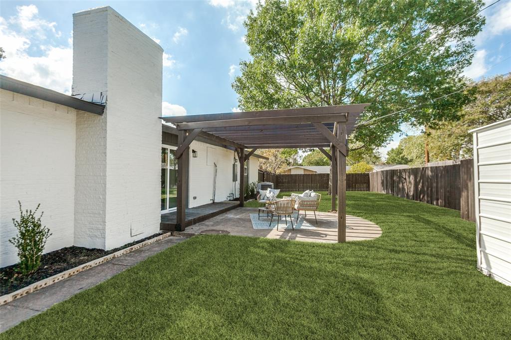 Backyard featuring a concrete patio, a covered wooden pergola, a white masonry chimney, and a fenced-in lawn