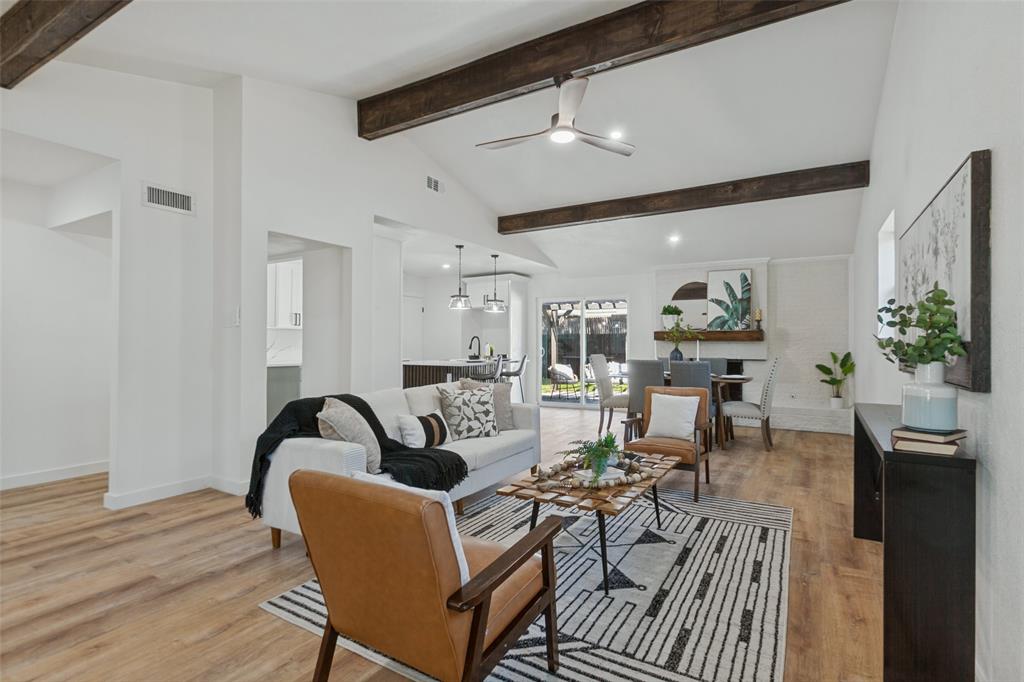 Vaulted ceilings featuring exposed decorative beams, wood-finish flooring, a painted brick fireplace, and integrated ceiling fan