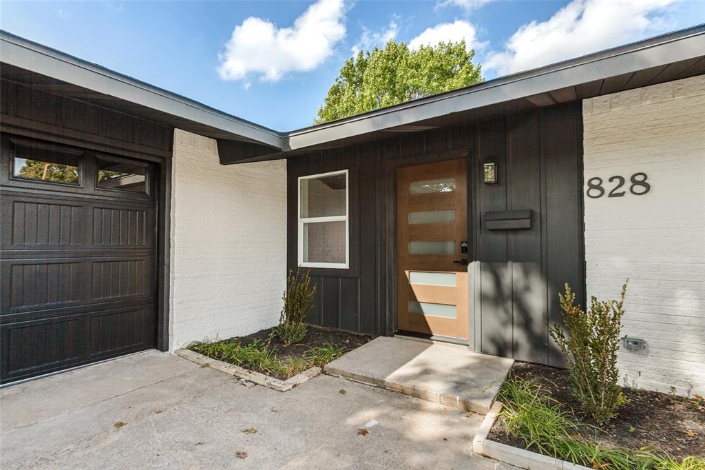 Exterior entry featuring a contrast-painted brick and wood-panel facade, multi-panel garage door, modern wood-tone door with horizontal glass inserts, and concrete hardscaping