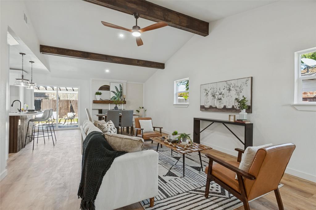 Vaulted ceilings featuring stained wood beams, light-tone wood-finish flooring, and sliding glass doors with access to the outdoors