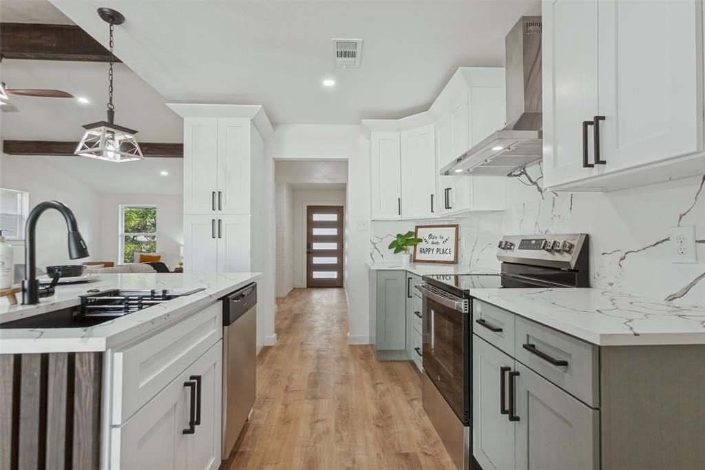 Kitchen featuring white shaker-style cabinetry, two-tone lower sage cabinetry, quartz countertops with veining, full-height decorative backsplash, and wood-finish flooring