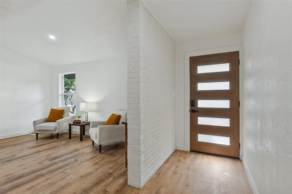 Entryway featuring a wood-finish front door with horizontal frosted glass panels, white painted brick accent wall, and wood-finish flooring