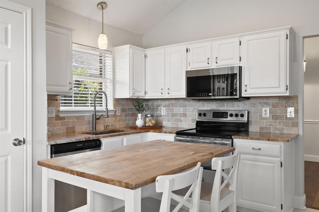 Kitchen featuring white shaker-style cabinetry, stone tile backsplash, stone countertops, stainless steel appliances, and a central island with a wood surface