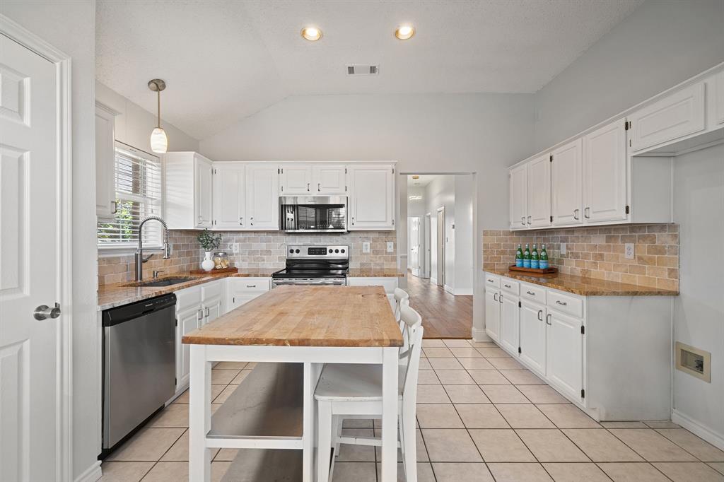 Kitchen featuring white cabinetry, stone-finish countertops, stainless steel appliances, brick-style backsplash, and a central island with a wood surface