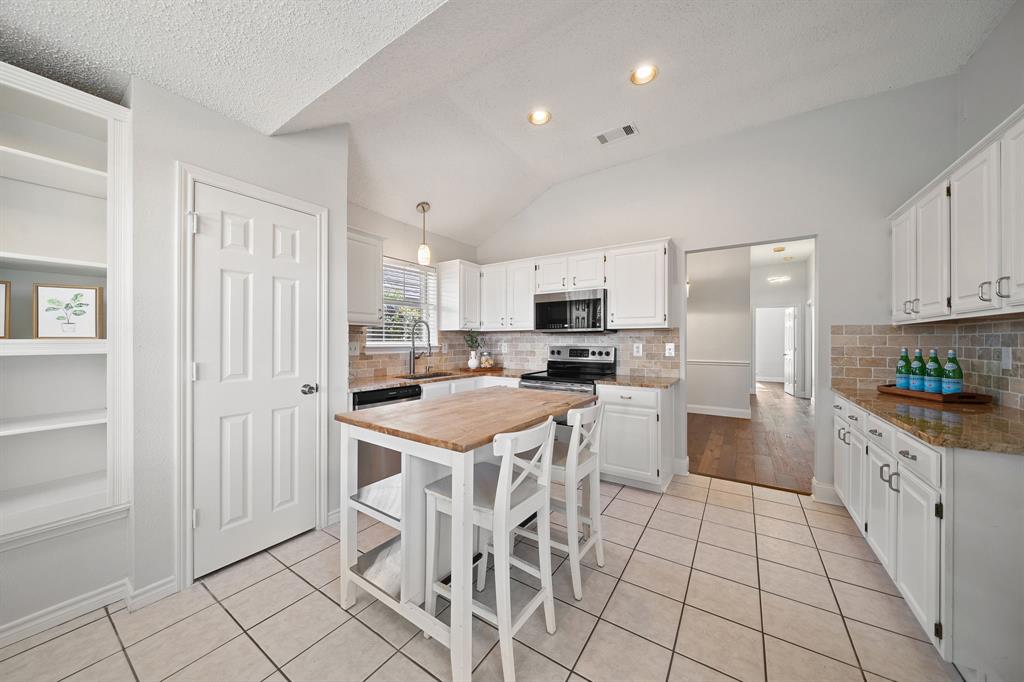Kitchen featuring white cabinetry, stone-surface countertops, a brick-style tile backsplash, vaulted ceiling, and built-in shelving