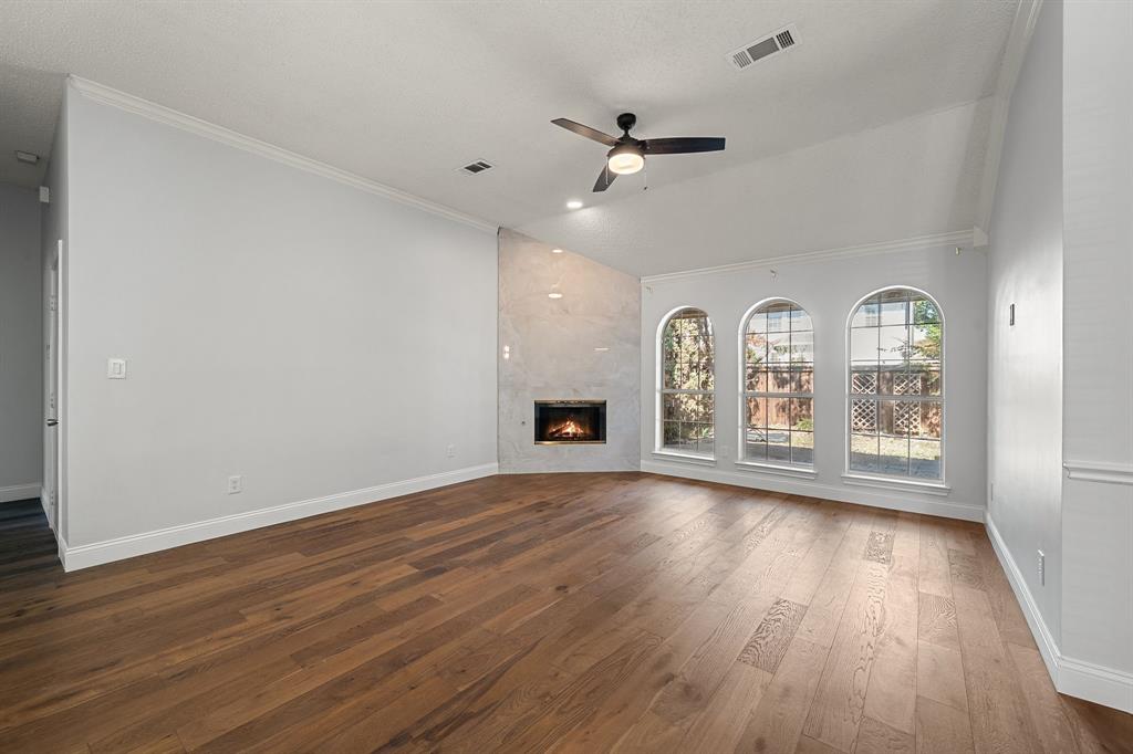 Vaulted ceilings, wood-finish flooring, corner fireplace with stone-surround facade, and three arched windows