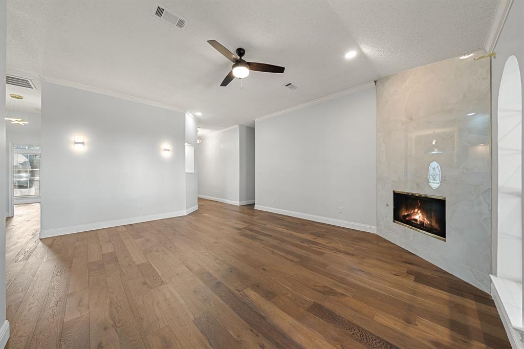 Living area featuring wood-finish flooring, a stone-surround fireplace, crown molding, a ceiling fan with light kit, and wall-mounted sconces